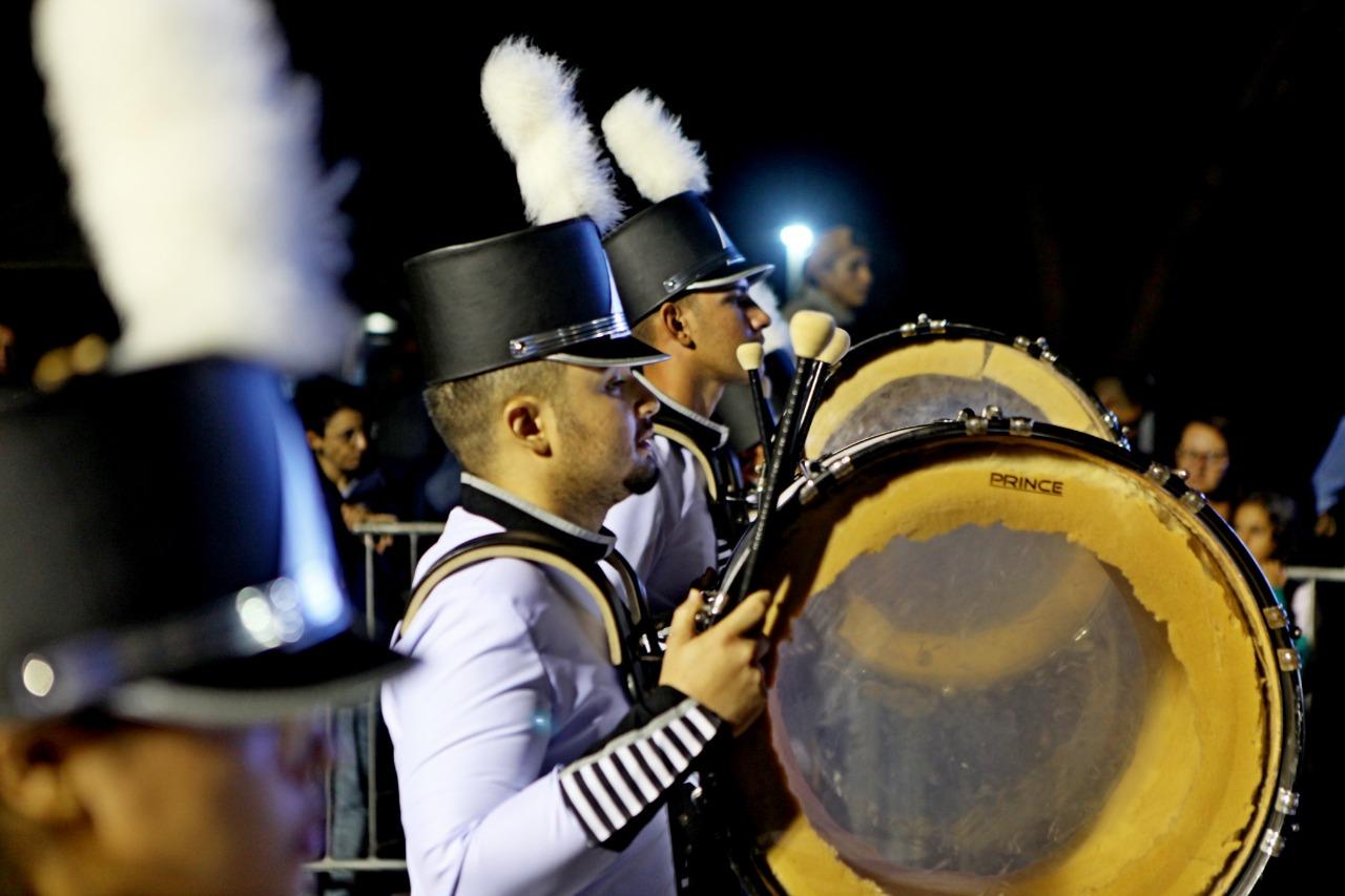 Fanfarra com chapéus de plumas e bumbo durante desfile noturno